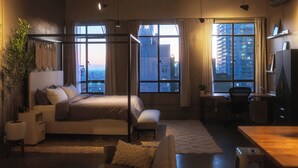 Habitación de hotel moderna con una cama grande, un escritorio y vistas a la ciudad a través de amplios ventanales.