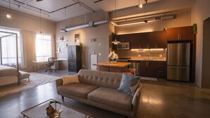 Una sala de estar moderna con un sofá, una mesa de centro y una cocina equipada con refrigerador, estufa y alacenas.