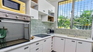 A compact kitchen with a microwave, oven, and sink. There is a window with a view of greenery outside.