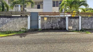 A modern two-story building with a gated entrance, a concrete wall, and a gravel driveway.