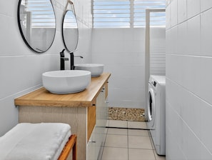 Een moderne badkamer met twee wastafels, een houten aanrechtblad, een spiegel, een handdoek, een wasmachine en een betegelde vloer.