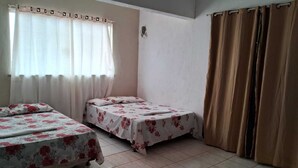 Habitació amb dos llits, una finestra amb cortines fines i una cortina marró.