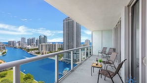 Un balcón con vistas a un río y al paisaje urbano, amueblado con sillas y una mesa.