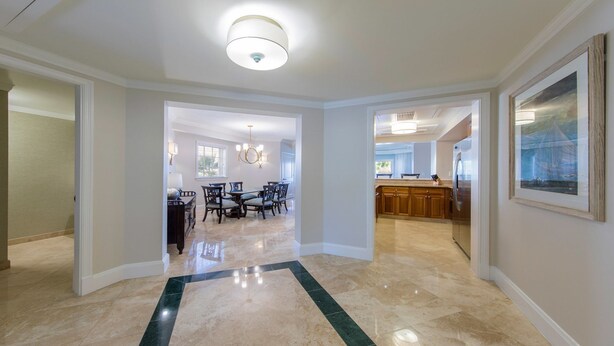 A spacious hallway with a marble floor, leading to a dining area with a chandelier and a kitchen with wooden cabinets and a stainless steel refrigerator. - Newly renovated luxurious 2 bedroom 2 1/2 bath beachfront condo. (St Thomas)