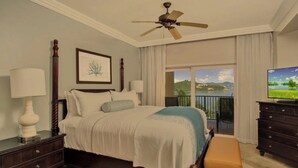 A bedroom with a bed, bedside tables, a ceiling fan, a TV, and a balcony with a view of the landscape. - Newly renovated luxurious 2 bedroom 2 1/2 bath beachfront condo. (St Thomas)