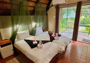 A hotel room with a bed, a nightstand, a window with curtains, and a view of greenery outside. - Ngandu Hotel - Rundu (Rundu)