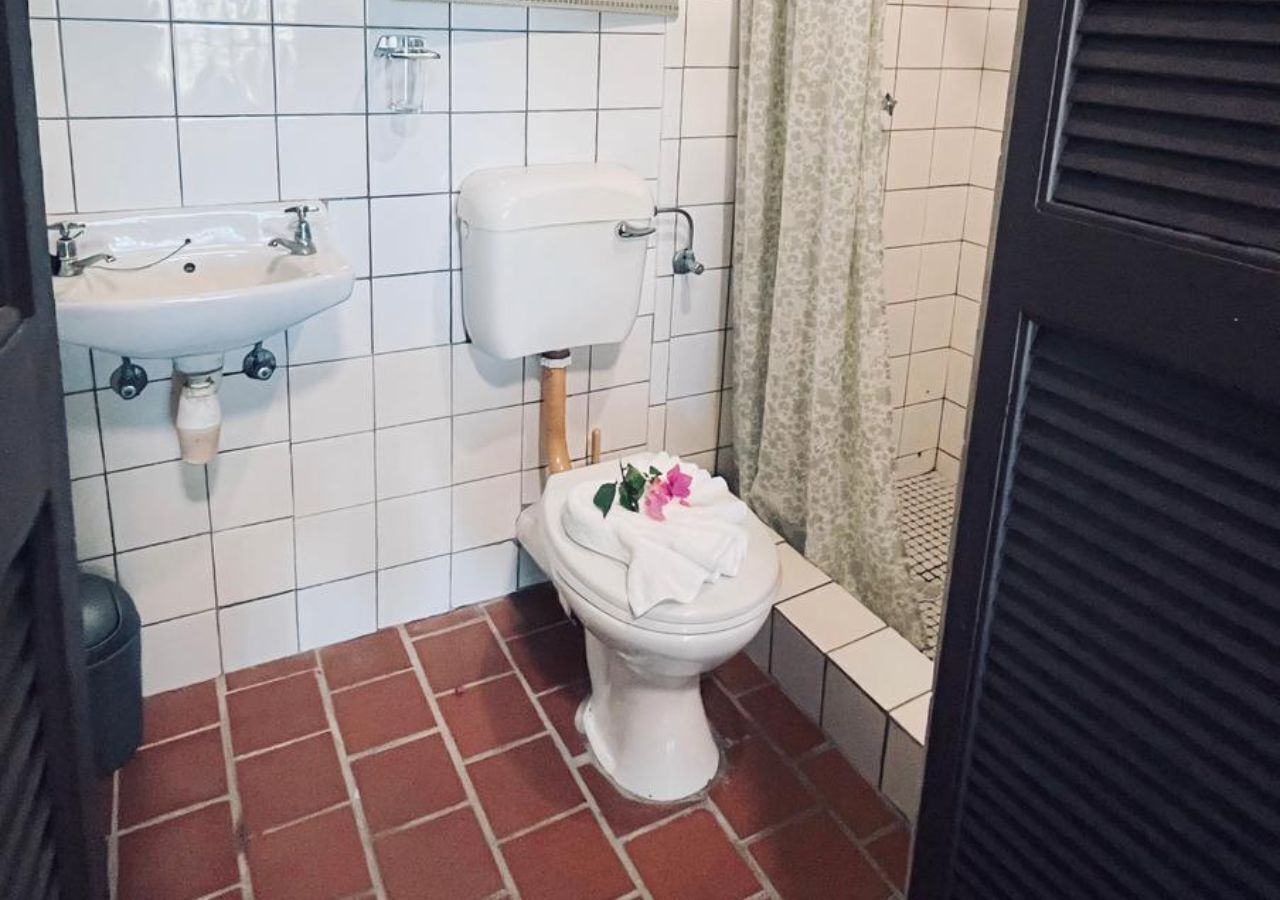 Egy fürdőszoba, amelyben fehér WC-csésze, fehér mosdókagyló és WC-papírtartó található.