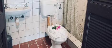 Egy fürdőszoba, amelyben fehér WC-csésze, fehér mosdókagyló és WC-papírtartó található.