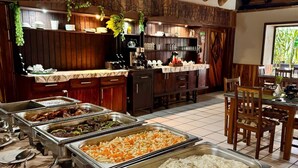 A buffet setup with various food options, a wooden interior, and a dining area with chairs and tables.