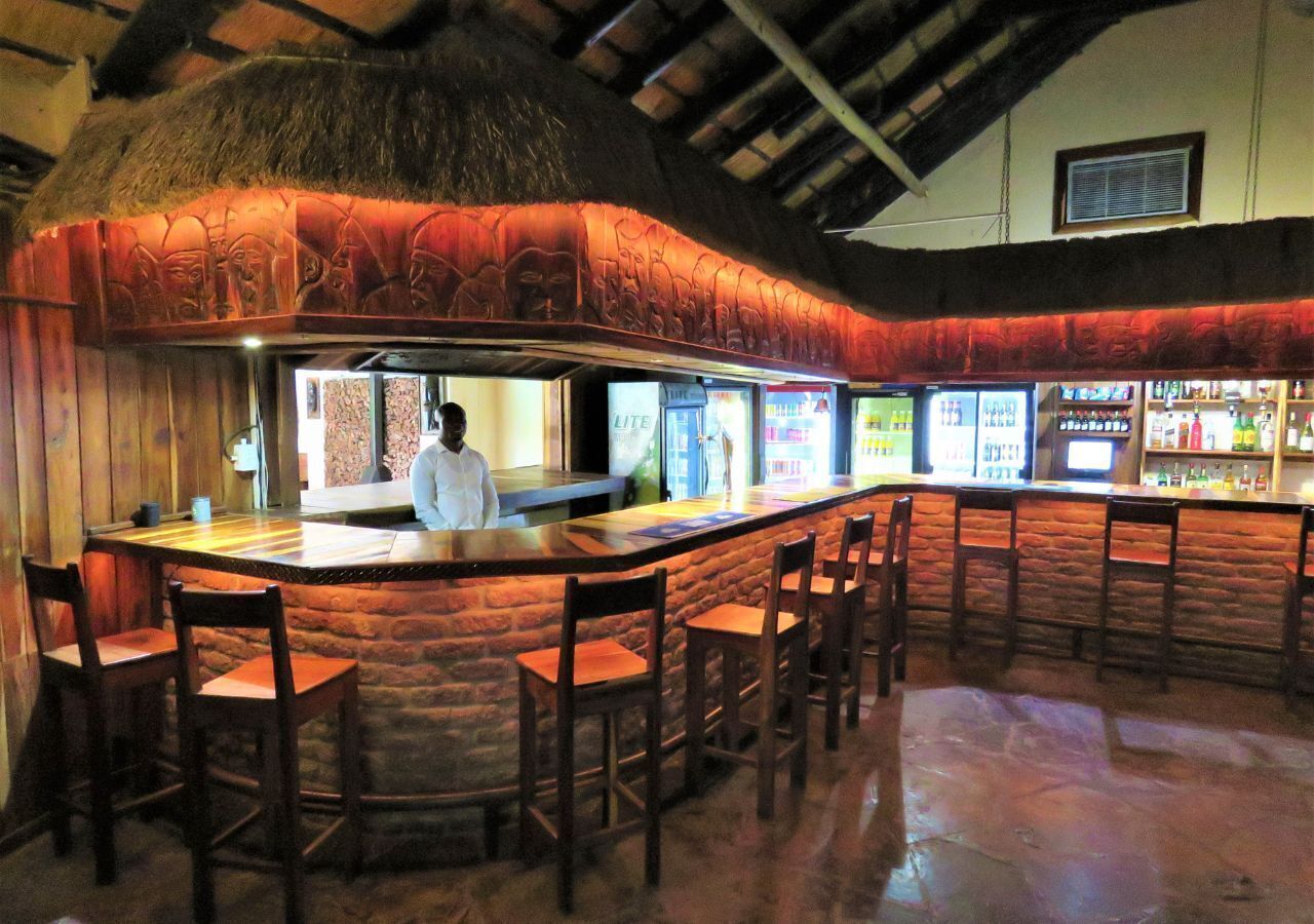 A bar area with a stone counter, wooden chairs, and a thatched roof.