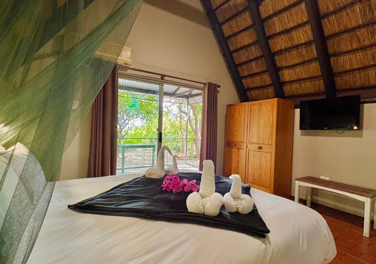 A bedroom with a bed, a wooden wardrobe, a television on the wall, and a window with curtains.