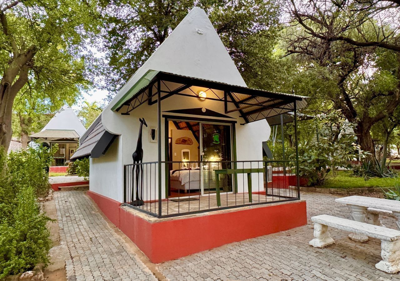 Un edificio pequeño de color blanco, con base roja y techo negro. Tiene un porche cubierto con barandilla y un banco.
