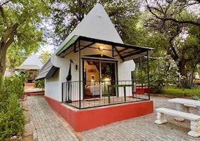 A small, white building with a red base and a black roof. It has a covered porch with a railing and a bench.