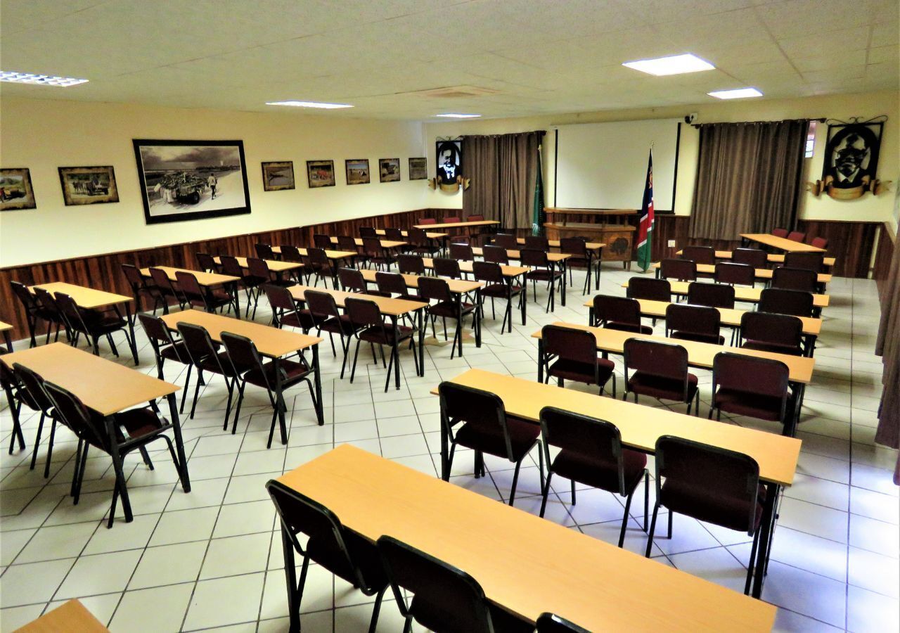 Un aula con filas de escritorios y sillas, una pantalla de proyector y una bandera.