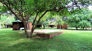 A grassy area with a brick structure, possibly a pavilion, surrounded by trees.