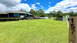 A residential property with a well-maintained lawn, a house with a large garage, and a number sign '157' indicating the property number. - Family Home on Golden Bay Farm — Peaceful, Kid-Friendly Stay (Puramāhoi)