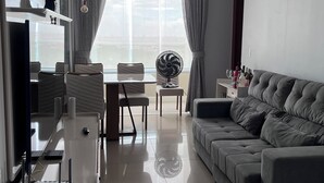 Un salon moderne avec un canapé gris, un coin repas comprenant une table et des chaises, un téléviseur et une grande fenêtre avec des rideaux.