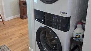 Un lavadero compacto y moderno con lavadora y secadora de carga frontal, suelo de madera y una alfombra decorativa.