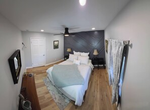 A bedroom with a bed, bedside tables, a ceiling fan, a door, and a framed picture on the wall.