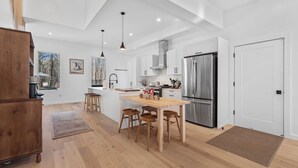 Eine moderne Küche mit weißen Schränken, einem Edelstahl-Kühlschrank, Holzstühlen und einer großen Kochinsel.