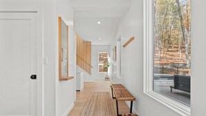 A modern hallway with a wooden bench, a woven rug, and a large window with a view of trees. - Woodstock Ridge / Hot Tub, Pool & Fire Pit (Woodstock)
