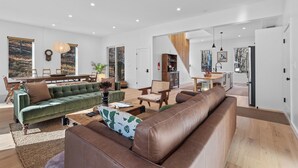 A spacious living area with a green sofa, brown leather couch, and wooden flooring. There is a dining area with a table and chairs, and a kitchen in the background. - Woodstock Ridge / Hot Tub, Pool & Fire Pit (Woodstock)