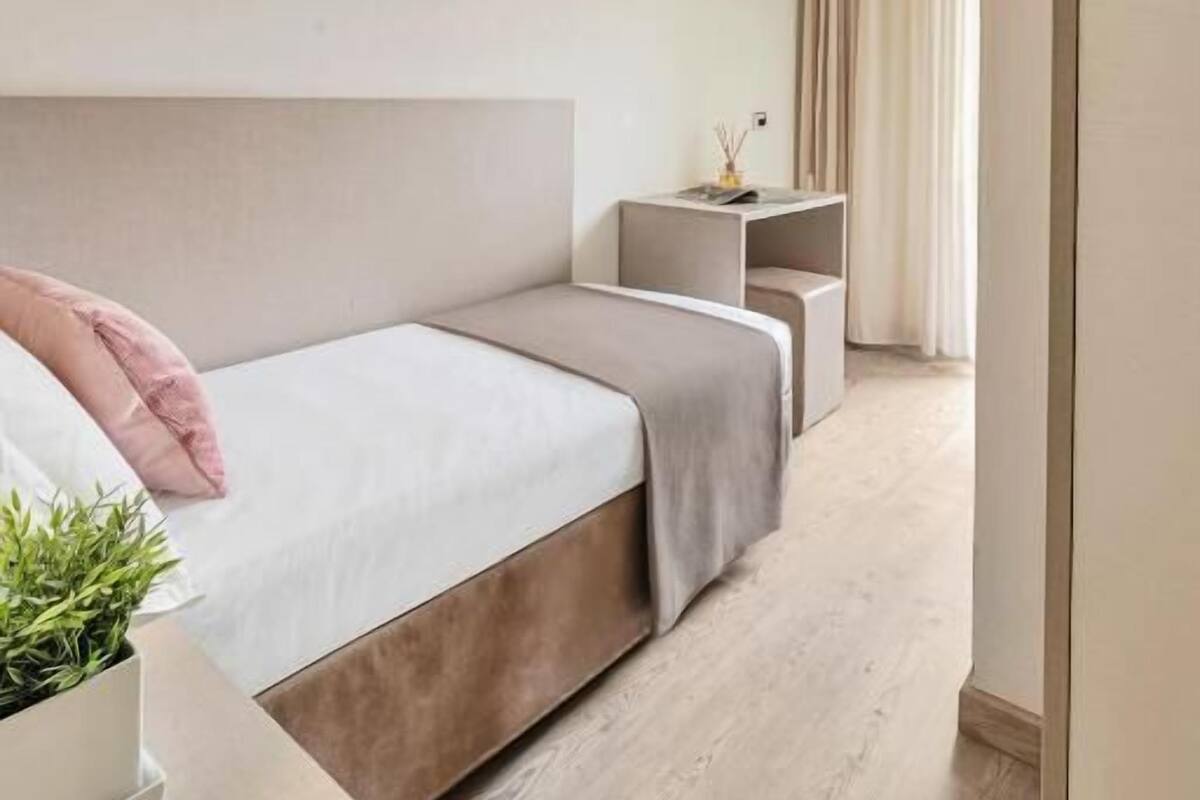 A modern hotel room with a large bed, bedside tables, a flat-screen TV, and a small plant.
