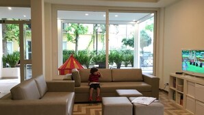 A modern living room with a sofa, ottomans, and a television. - Hotel Lux (Gabicce Mare)