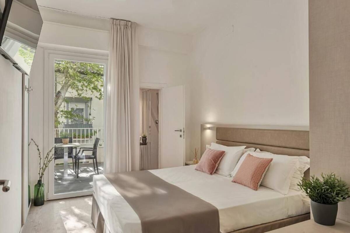 A modern bedroom with a large bed, a sliding glass door to a balcony, and a small table with chairs.