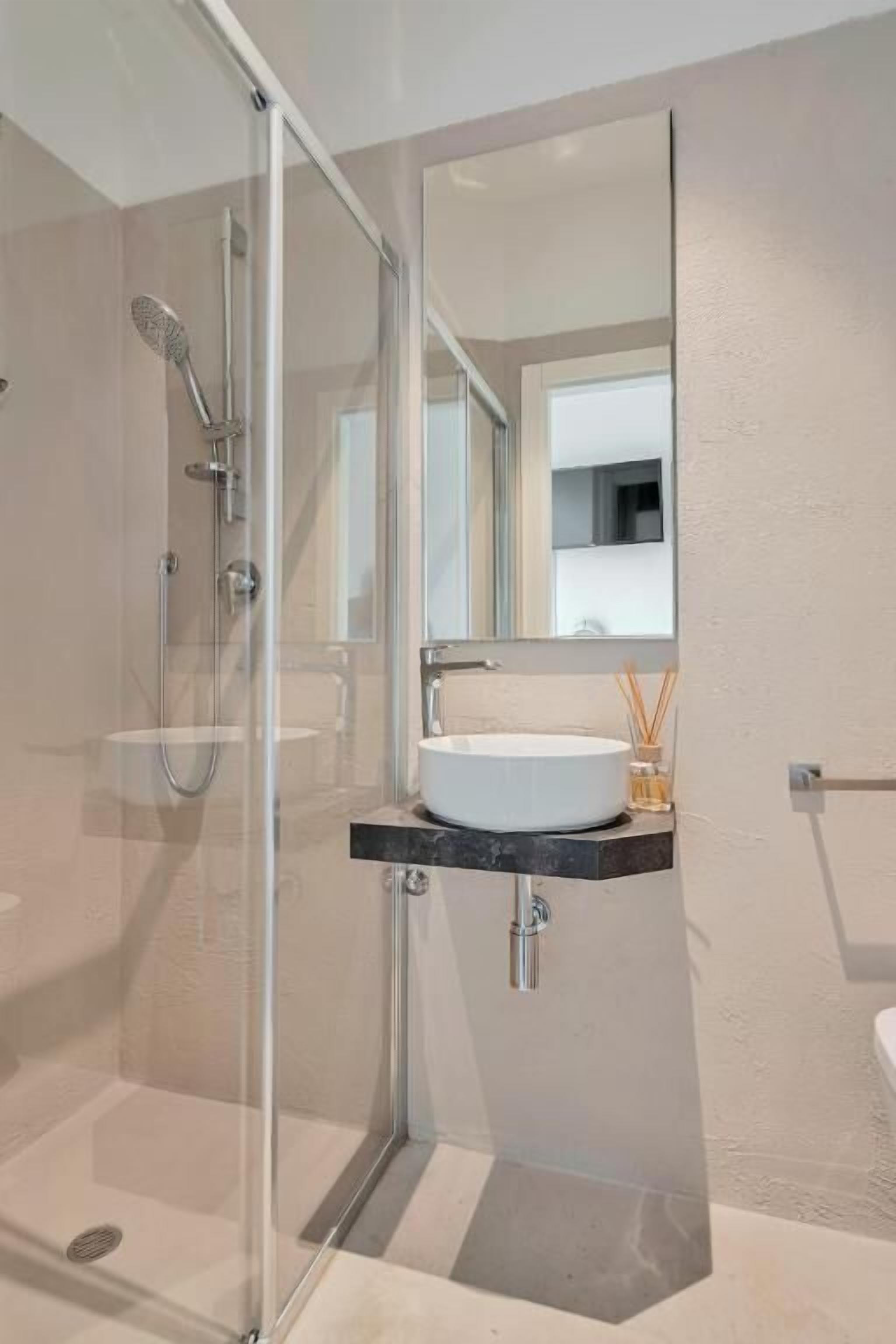 A modern bathroom with a glass-enclosed shower, a white sink, and a mirror above the sink.