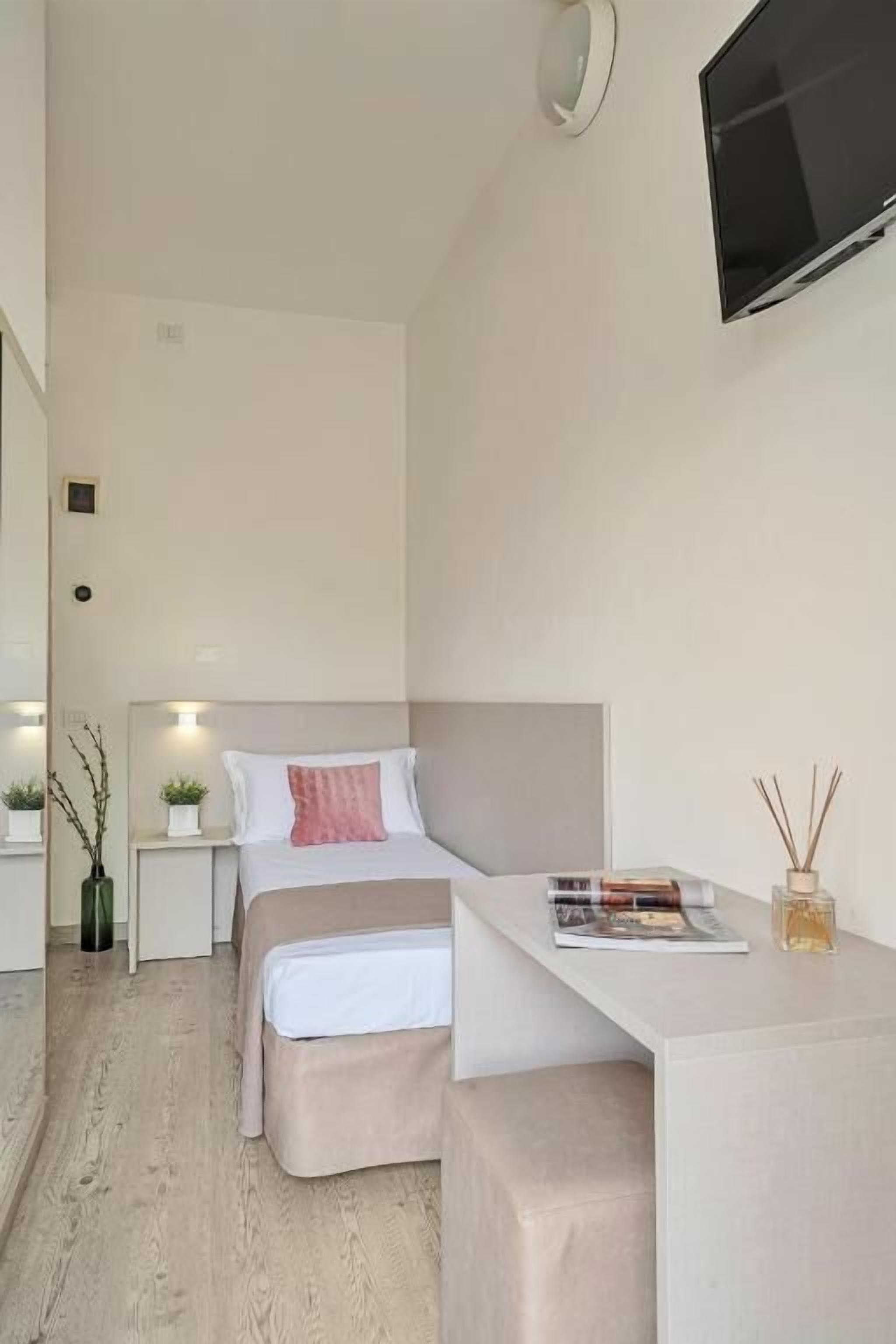 A modern hotel room with a bed, bedside table, and a mounted TV.