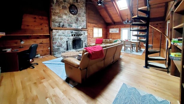 Un interior de cabaña acogedor con chimenea de piedra, paredes de madera, un sofá y una escalera de caracol.