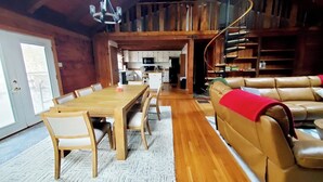 Un espacio habitable amplio con una mesa de comedor de madera, sillas acolchadas, un sofá de cuero y una escalera que conduce a un nivel superior.