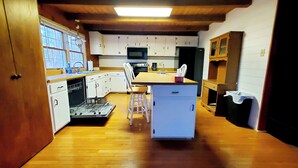 Una cocina compacta con suelo de madera, muebles blancos, una isla central y un microondas sobre el fregadero.