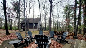 Una cabaña rústica rodeada de un bosque. Varias sillas Adirondack están dispuestas alrededor de una mesa de madera.