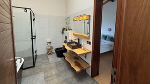 Ein modernes Badezimmer mit Dusche, Toilette und Waschbecken. Auf dem Boden befindet sich eine hölzerne Bank und ein kleiner Teppich.