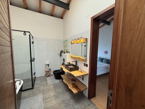 Ein modernes Badezimmer mit Dusche, Toilette und Waschbecken. Auf dem Boden befindet sich eine hölzerne Bank und ein kleiner Teppich.