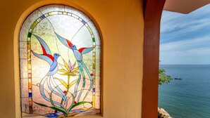 A stained glass window with birds and flowers, a coastal view, and a clear sky.