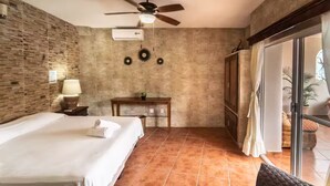 A hotel room with a bed, a desk, a ceiling fan, and a view through a glass door.