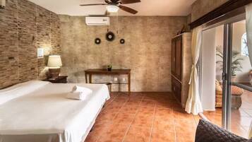 Une chambre d’hôtel avec un lit, un bureau, un ventilateur de plafond et une vue sur l’extérieur, visible à travers une porte vitrée.
