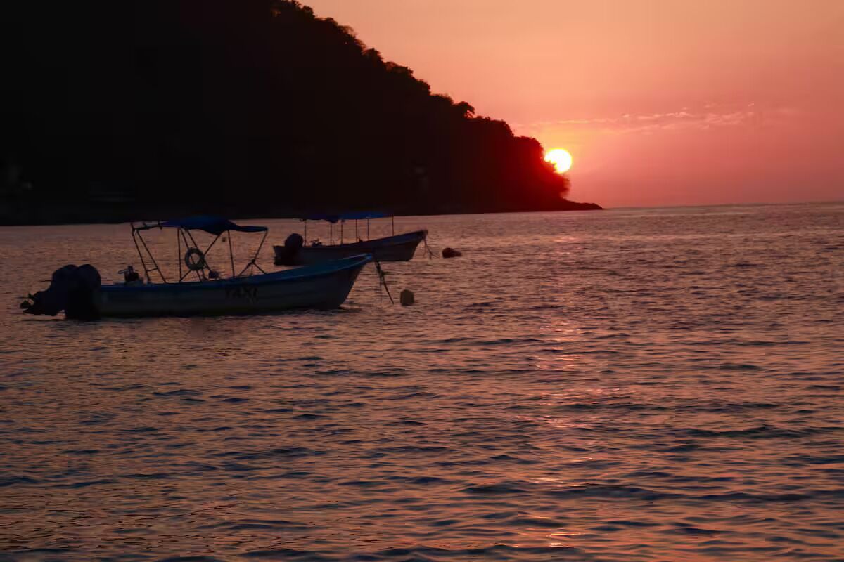 Ruhige Wasserfläche mit Booten und einem Sonnenuntergang.