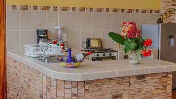 Une cuisine avec un mur recouvert de carreaux, une cuisinière à gaz, un grille-pain, une machine à café et un vase décoratif avec des fleurs.