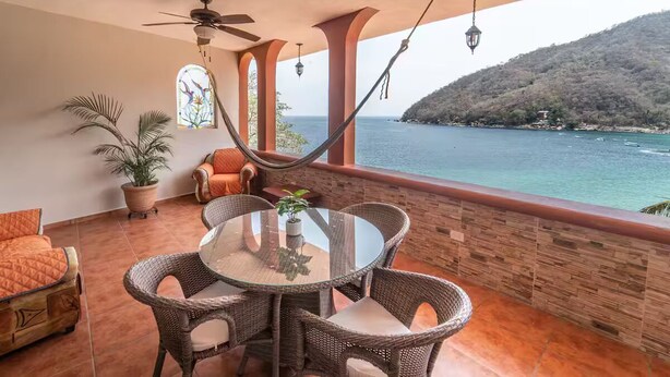 A balcony with wicker furniture, a glass table, and a view of the sea.