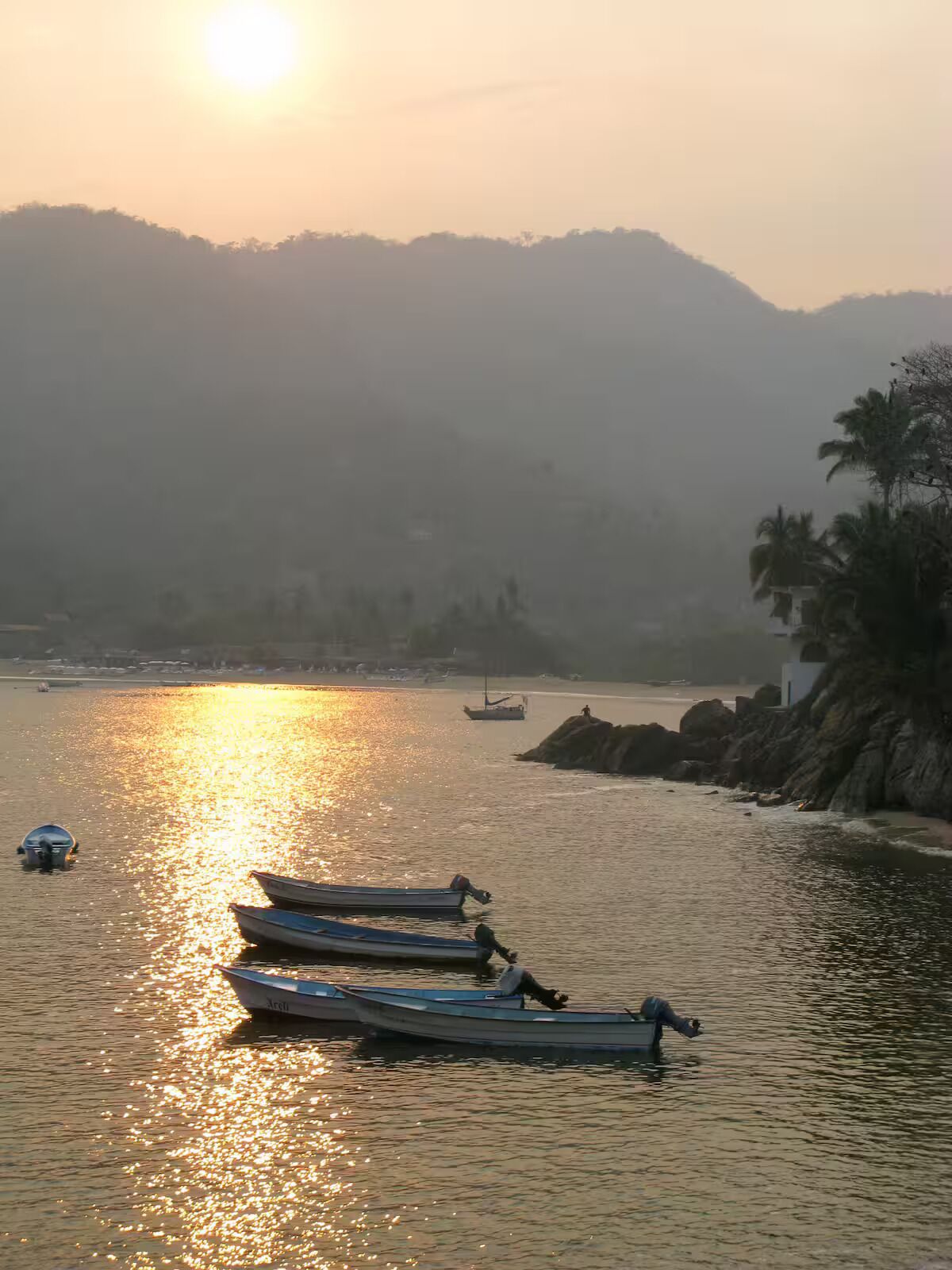 Un lac paisible au coucher du soleil, avec des bateaux et une rive rocheuse.
