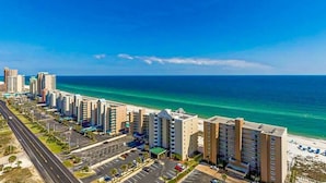A coastal hotel with multiple high-rise buildings, a parking lot, and a beach in the background. - Crystal Tower 1802: 2BR Condo (Gulf Shores)