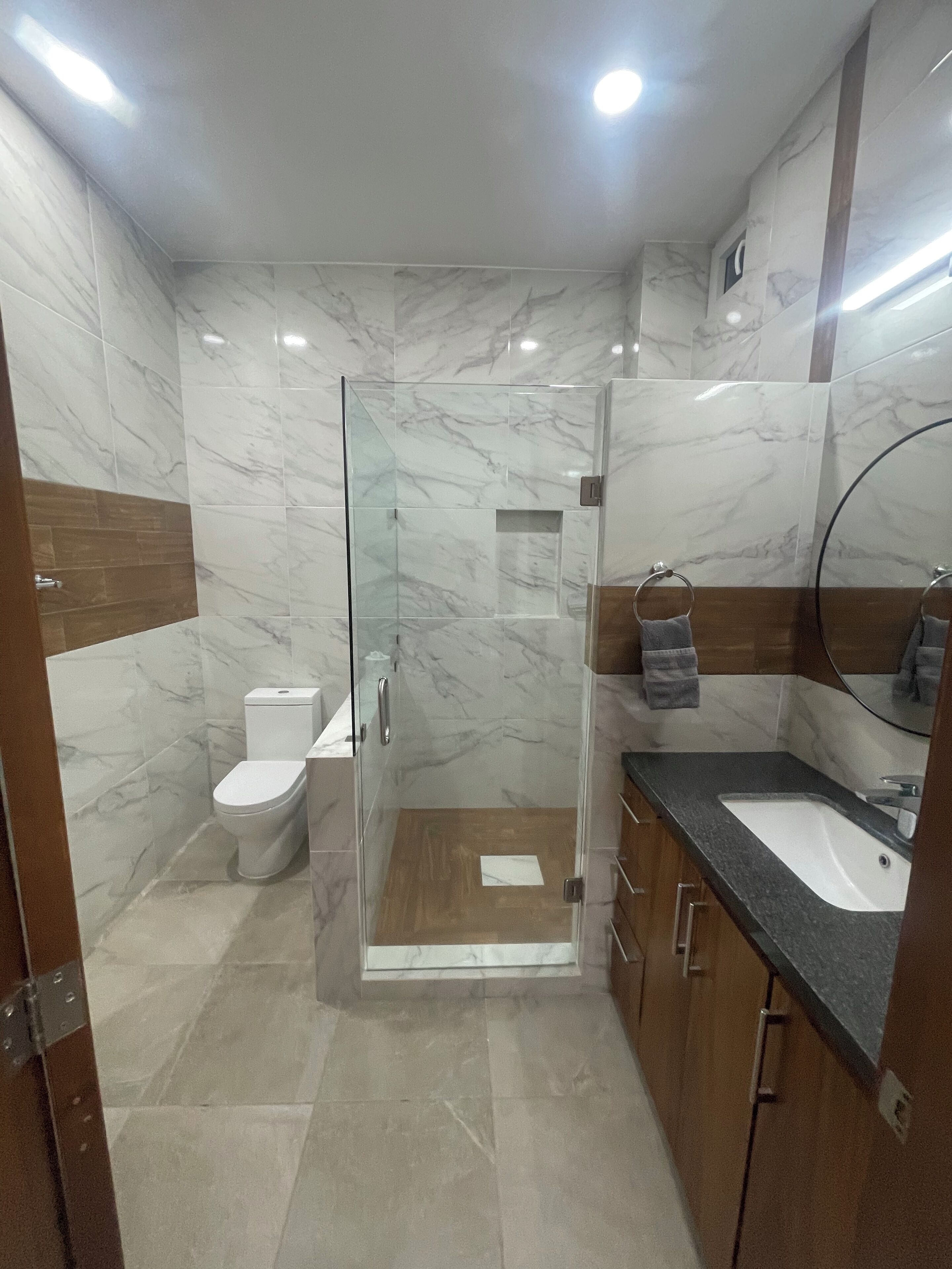 Une salle de bain moderne avec une douche à parois de verre, des toilettes et un meuble-lavabo avec un évier et un miroir.