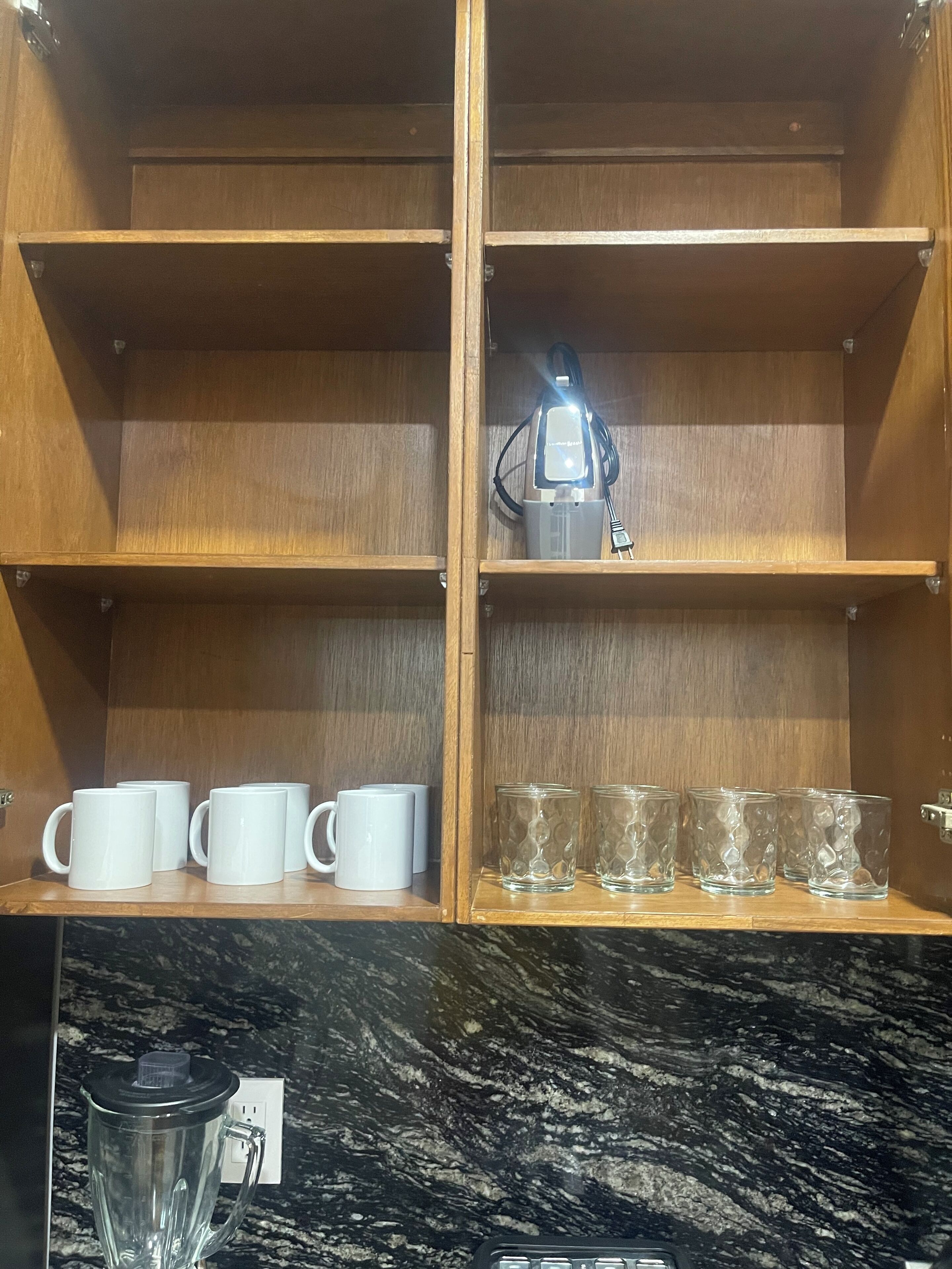 A wooden cabinet with two shelves, one holding white mugs and the other holding clear glasses.