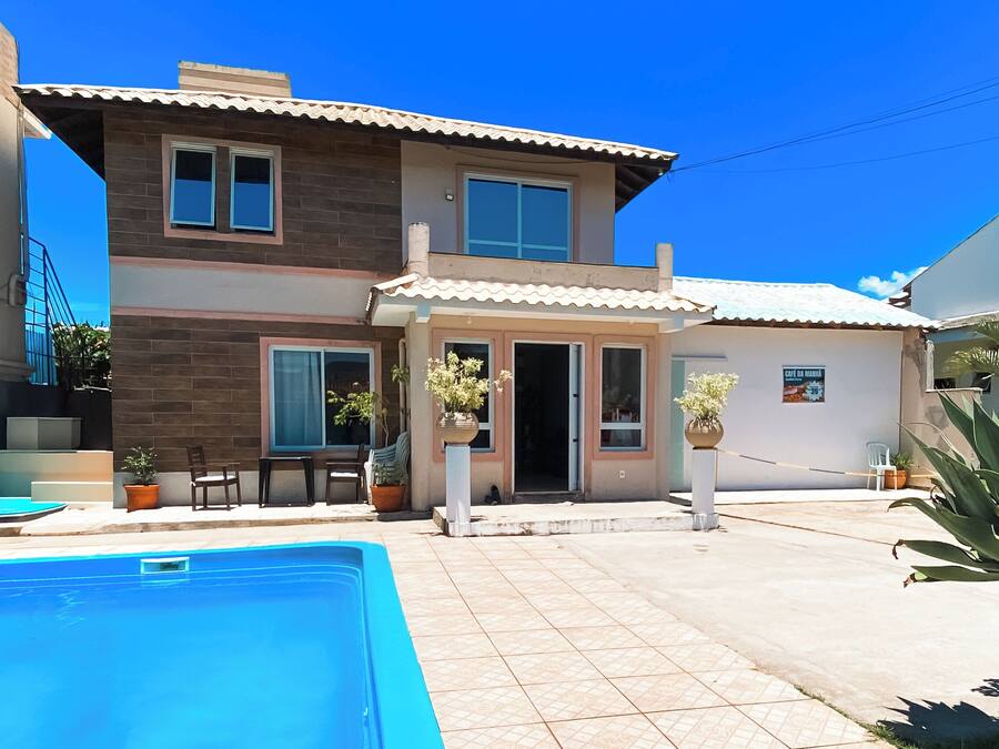 A two-story house with a swimming pool, outdoor seating, and potted plants.
