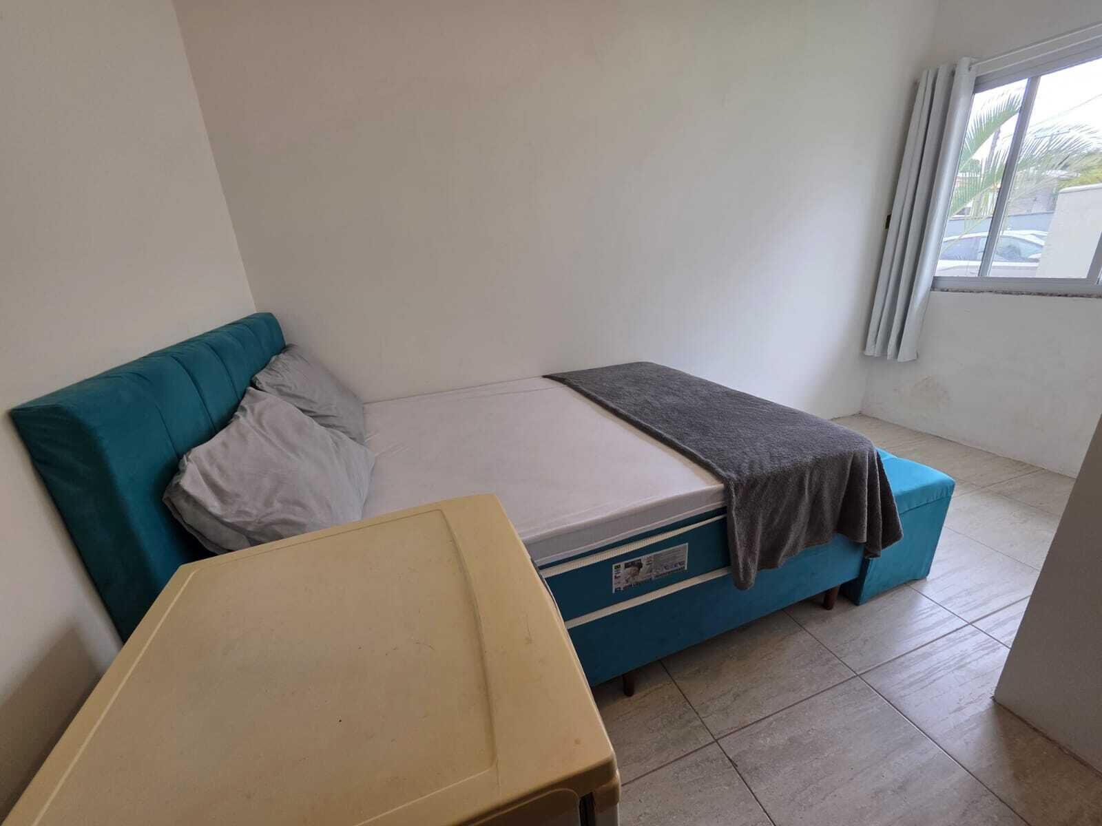 Una habitación pequeña con cama individual, sofá azul, una mesita y una ventana con cortinas.