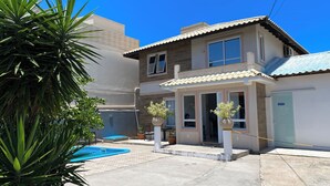 A two-story house with a swimming pool, potted plants, and a clear blue sky. - Hostel Papai (Florianopolis)